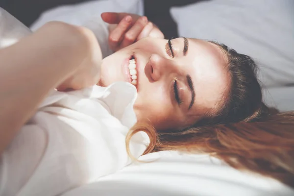 Mujer bonita en la cama en el apartamento moderno sonriendo y estirándose después de despertar —  Fotos de Stock