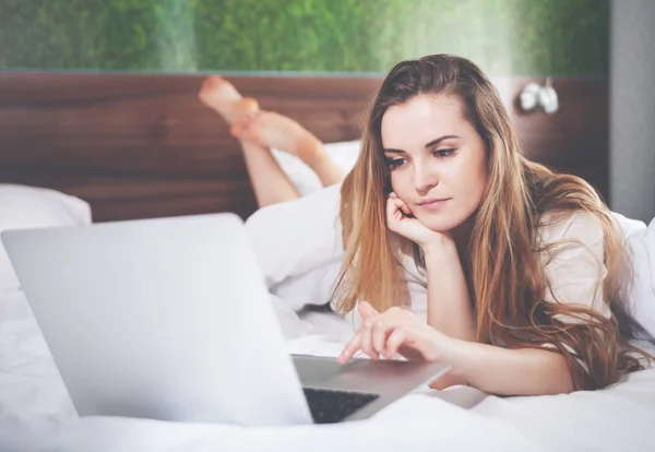 Mujer bonita en la cama en el apartamento moderno usando el ordenador portátil después de despertar —  Fotos de Stock