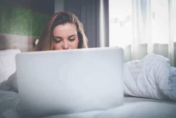 Mujer bonita en la cama en el apartamento moderno usando el ordenador portátil después de despertar —  Fotos de Stock