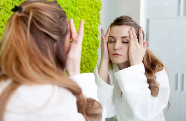 Красива жінка дивиться на дзеркало в сучасній ванній кімнаті і аплодує крем на обличчі — стокове фото
