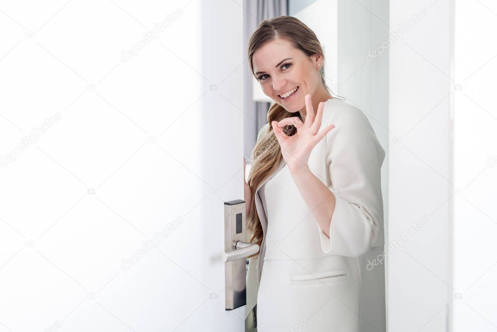 Pretty woman standing in doorway and making OK sign with her hand