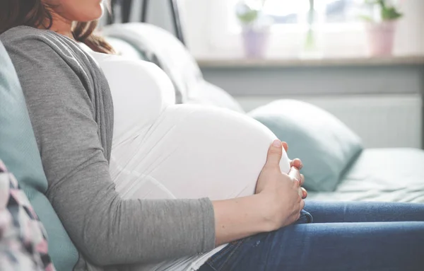 Беременная женщина сидит дома на диване вблизи живота — стоковое фото