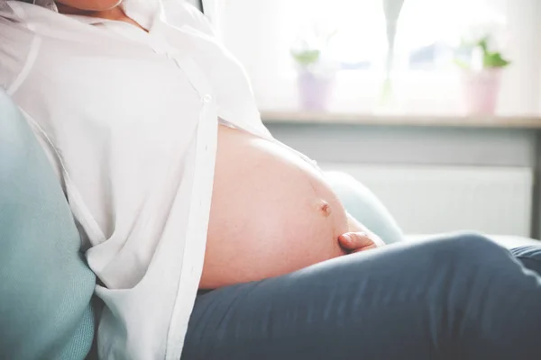 Schwangere sitzt zu Hause auf Sofa in Großaufnahme des Bauches — Stockfoto