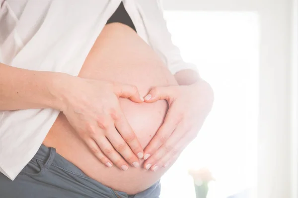 Schwangere hält zu Hause Hände in Herzform am Bauch — Stockfoto