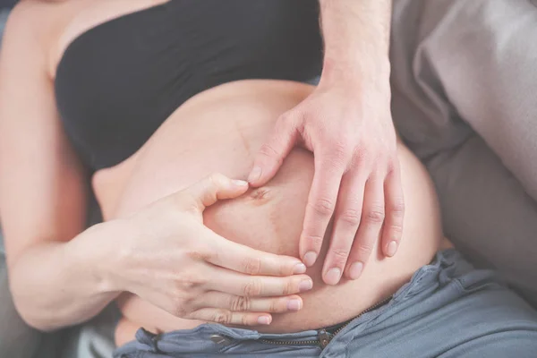 W ciąży brzuch i rodzice rąk w kształcie serca na brzuch w domu z bliska — Zdjęcie stockowe