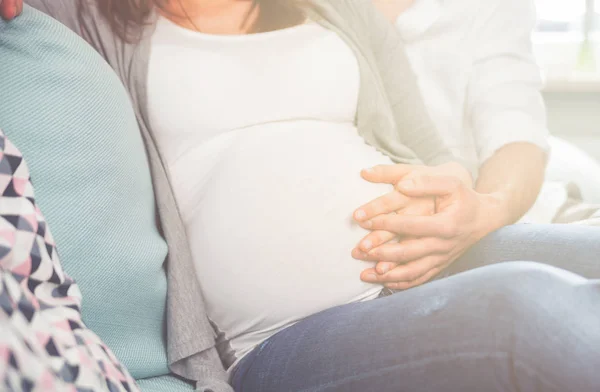 Buik van zwangere vrouw zittend op de Bank thuis — Stockfoto