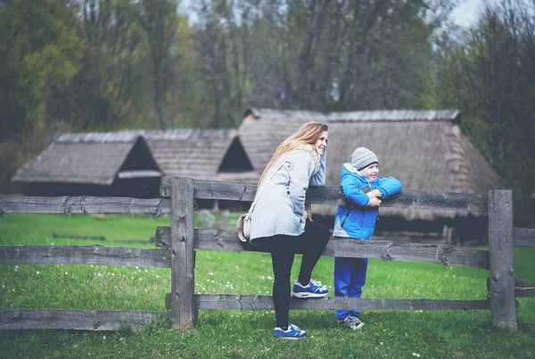 Mother and son resting near wooden fence in the countryside with old houses — Stock Photo, Image