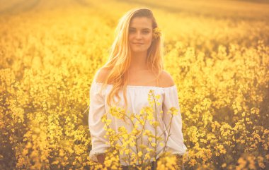 Gün batımında sarı kolza tohumu alanındaki gülümseyen kadın