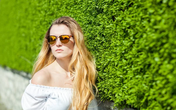 Menina com óculos de sol no fundo da sebe — Fotografia de Stock