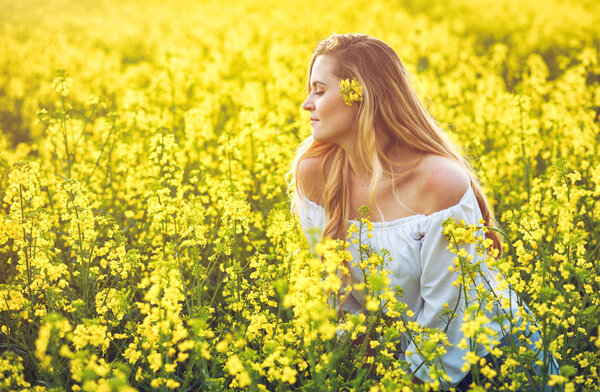 Smiling woman in yellow rapeseed field at sunny day
