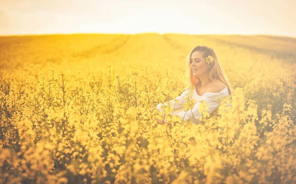 Усміхнена жінка в жовтому полі ріпаку на заході сонця — стокове фото