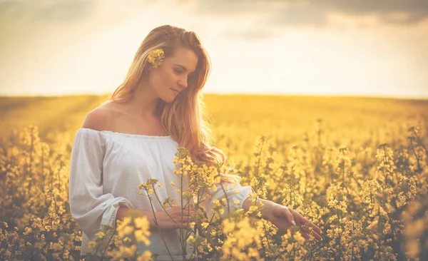 Mulher sorridente no campo de colza amarelo ao pôr do sol — Fotografia de Stock