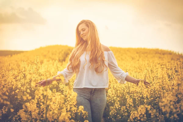 Mulher sorridente no campo de colza amarelo ao pôr do sol — Fotografia de Stock