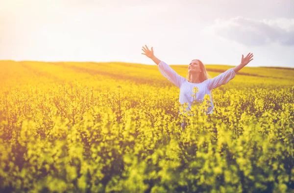 Femme souriante marchant dans le champ de colza jaune au coucher du soleil — Photo