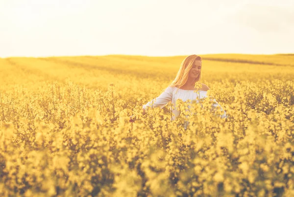 Sorrindo mulher andando no campo de colza amarelo ao pôr do sol — Fotografia de Stock
