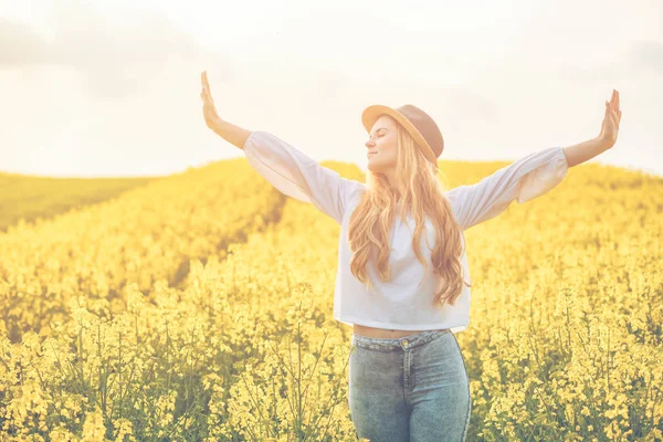 Femme souriante avec chapeau dans le champ de colza jaune au coucher du soleil — Photo