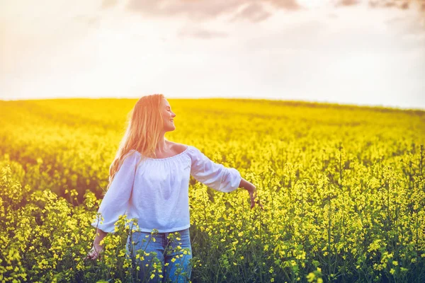 Mujer sonriente caminando en campo de colza amarillo al atardecer —  Fotos de Stock