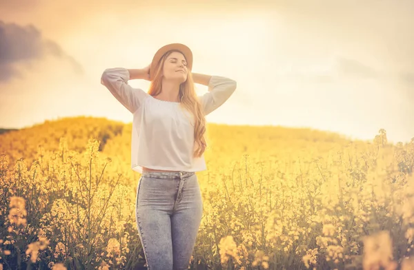 Mujer sonriente con sombrero en campo de colza amarillo al atardecer — Foto de Stock