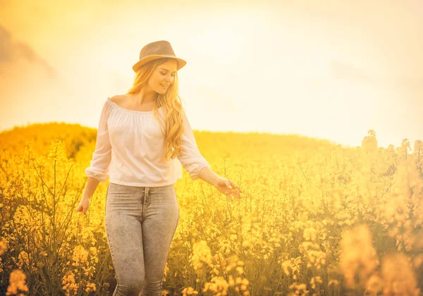 Mujer sonriente con sombrero en campo de colza amarillo al atardecer — Foto de Stock