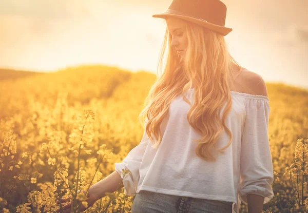 Mujer sonriente con sombrero en campo de colza amarillo al atardecer — Foto de Stock