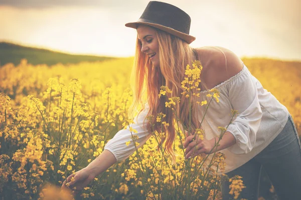 Улыбающаяся женщина в шляпе на желтом рапсовом поле на закате — стоковое фото
