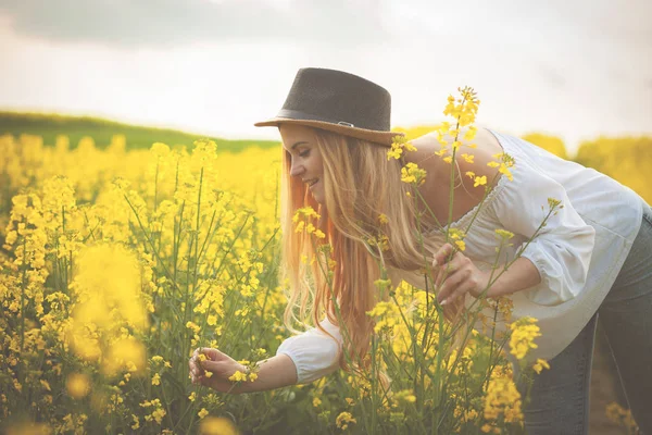 Mujer sonriente con sombrero en campo de colza amarillo al atardecer —  Fotos de Stock