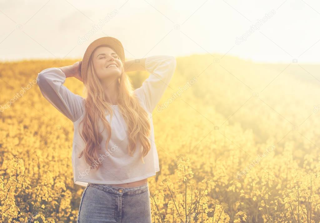 Smiling woman with hat in yellow rapeseed field at sunset