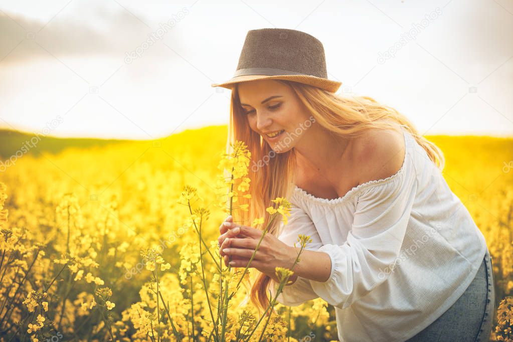 Smiling woman with hat in yellow rapeseed field at sunset