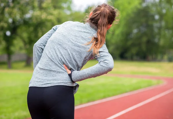 Mujer en pista de atletismo tiene calambres laterales durante el entrenamiento — Foto de Stock