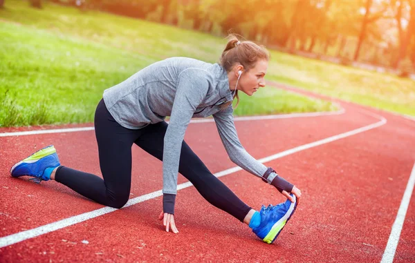 Mulher atlética em pista de corrida alongamento antes de treinar acessórios de fitness — Fotografia de Stock