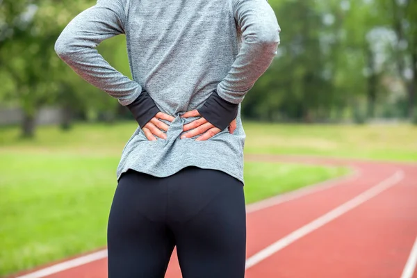 Athletic woman on running track touching hurt back with painful injury