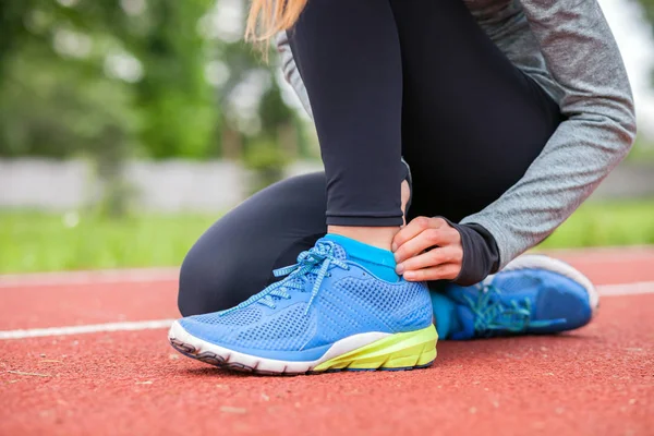 Athletic woman on running track touching hurt leg with ankle injury — Stock Photo, Image