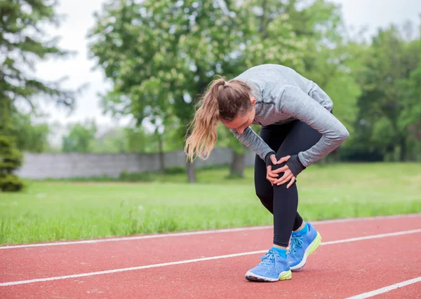 Спортивная женщина на беговой дорожке трогает больную ногу с травмой колена — стоковое фото