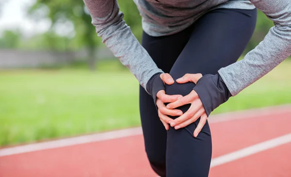 Athletic woman on running track touching hurt leg with knee injury — Stock Photo, Image