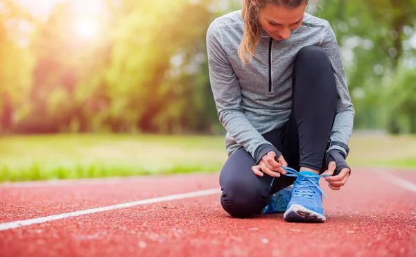 Спортивная женщина на беговой дорожке завязывает шнурки перед началом тренировки — стоковое фото