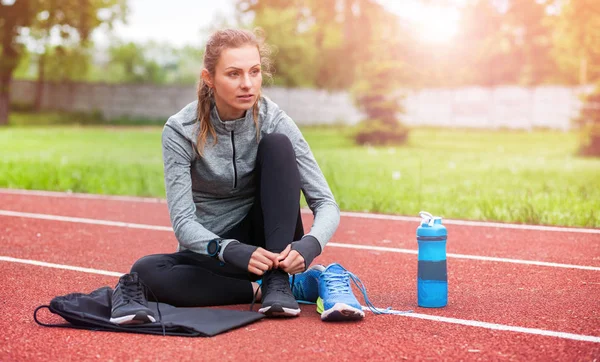 Athletische Frau auf der Laufstrecke schnürt Schnürschuhe, Fitness-Accessoires — Stockfoto