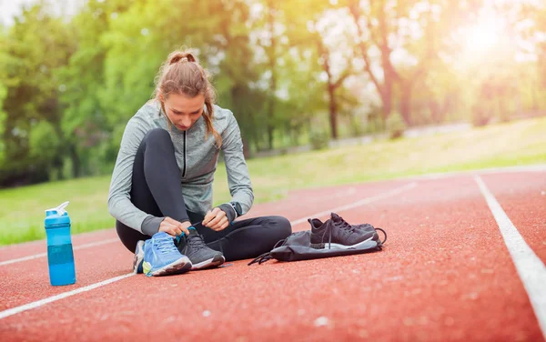 Спортивная женщина на беговой дорожке завязывая шнурки для обуви, фитнес аксессуары — стоковое фото