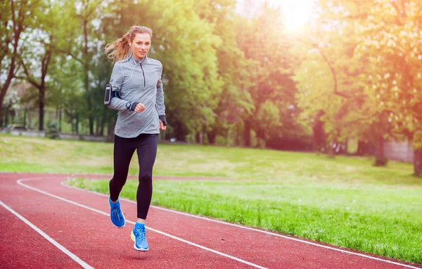 Sportovní žena běh na dráze s aplikace pro chytré telefony a hodinky, fitness životní styl — Stock fotografie