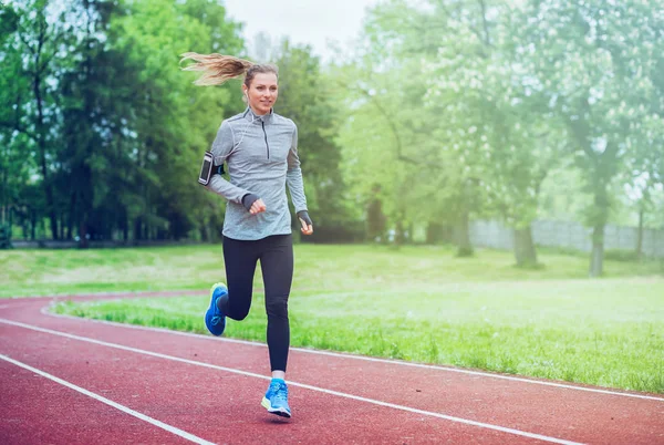 Athletic woman running on track with smart phone app, fitness lifestyle — Stock Photo, Image