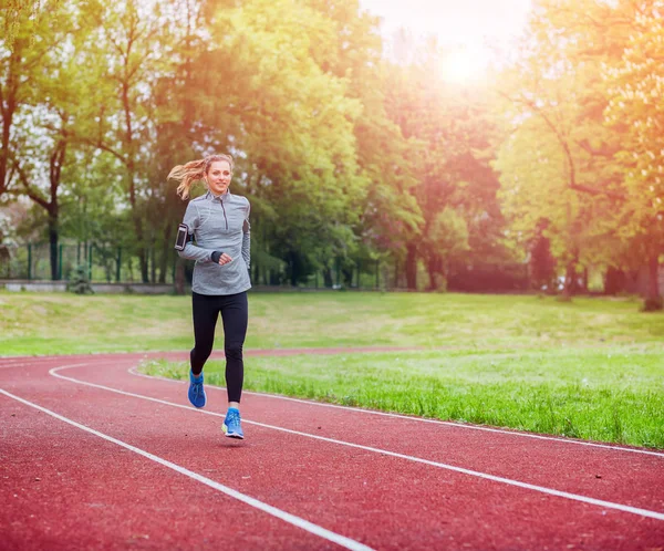 Sportovní žena běh na dráze s aplikace pro chytré telefony, fitness životní styl — Stock fotografie