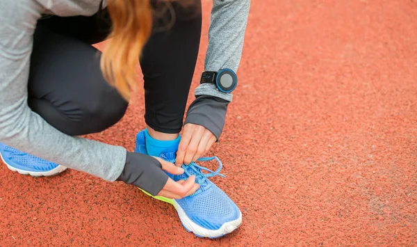 Mulher atlética com relógio inteligente na pista de corrida amarrar atacadores de sapatos — Fotografia de Stock