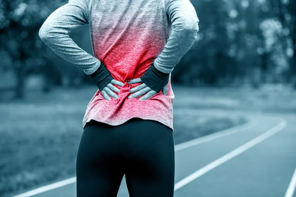 Athletic woman on running track touching hurt back with painful — Stock Photo, Image