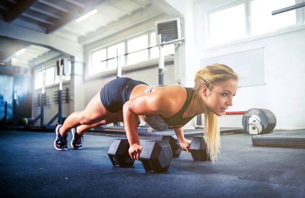 Vrouw uit te werken met halters doet push ups bij crossfit gym — Stockfoto