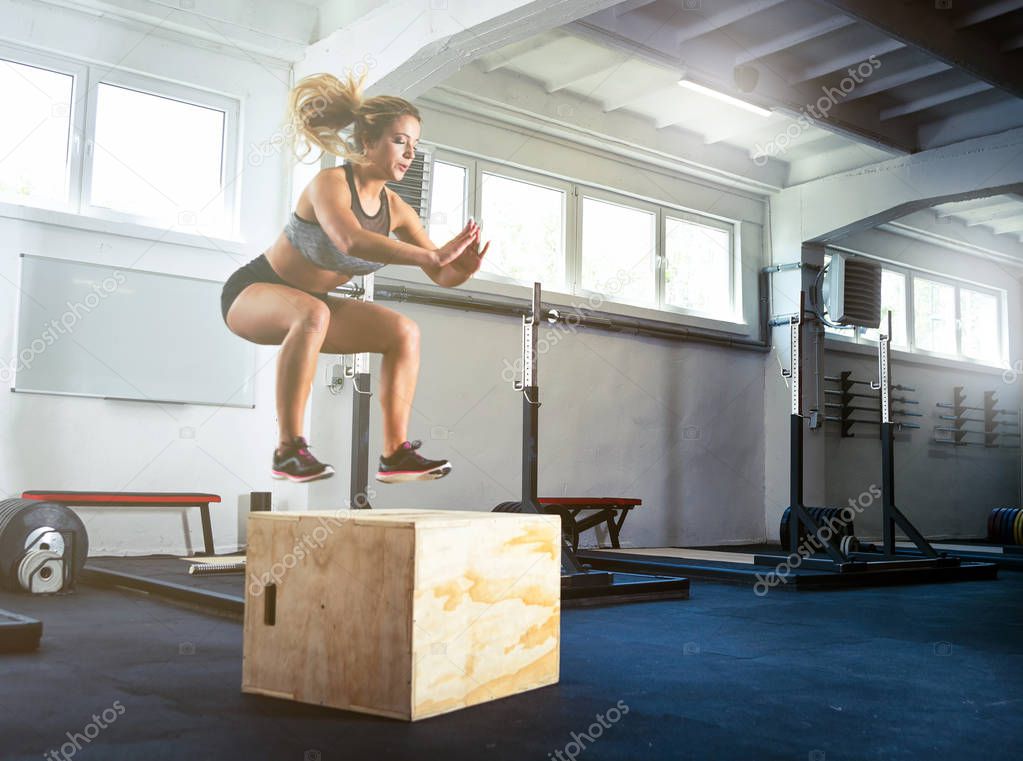 Fitness woman jumping on box training at gym