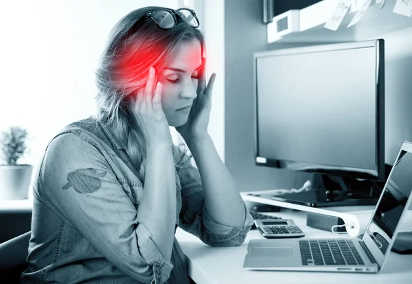 Женщина в домашнем офисе страдает от головной боли сидя за столом — стоковое фото