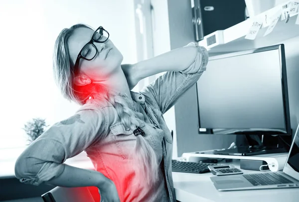 O femeie din biroul de acasă care suferă de dureri de spate stând la birou — Fotografie, imagine de stoc