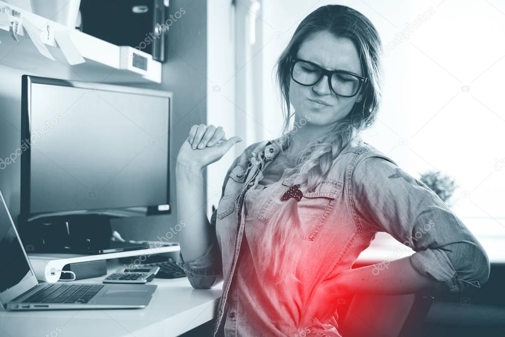 Woman in home office suffering from backache sitting at computer desk