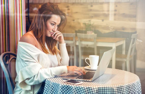 Деловая женщина, работающая с ноутбуком и мобильным телефоном в кафе, внештатная концепция — стоковое фото