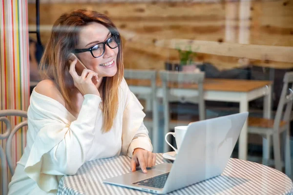 Ділова жінка, що працює з ноутбуком та мобільним телефоном у кафе, концепція фрілансу — стокове фото