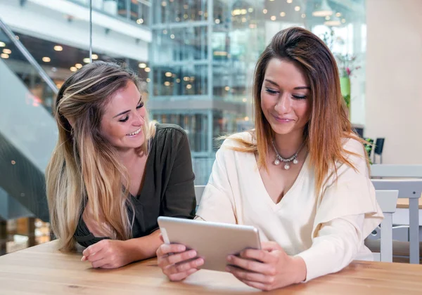 Dos chicas usando tableta digital viendo contenido multimedia en un café en un centro comercial — Foto de Stock